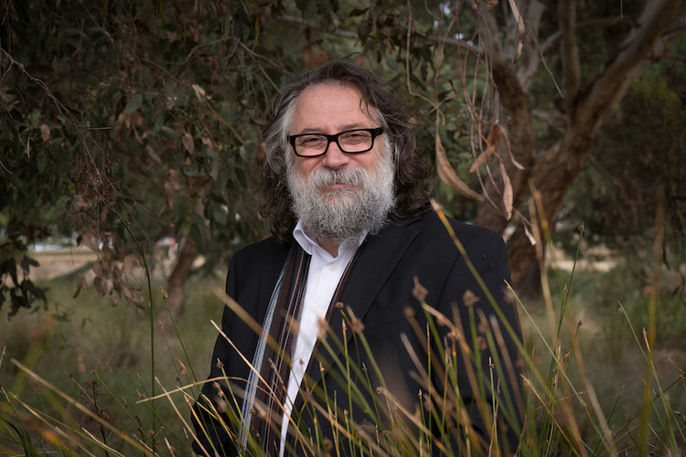 a man with a beard and glasses standing in a grassy area