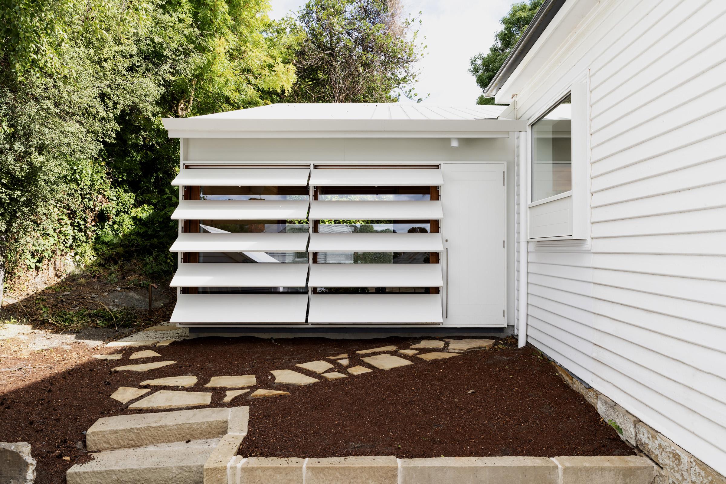 a white shed with a white wall and brown dirt around it