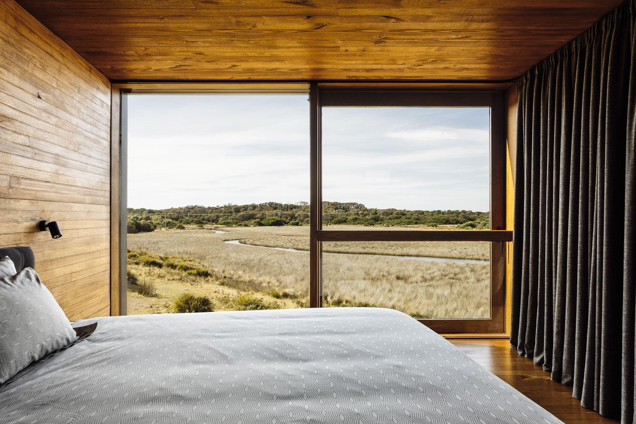a bed with a view of a field and a river through a window