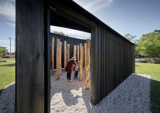 a woman and child standing in a room with wood poles