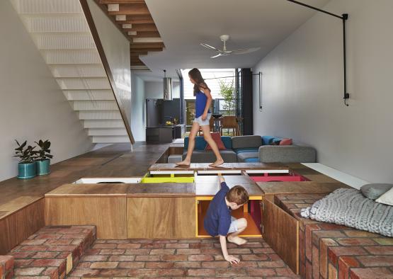 a boy and girl walking on a platform in a room with stairs