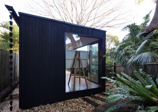 a black shed with a wooden easel in the middle of a yard