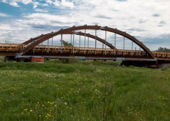 a bridge with a grass field and blue sky