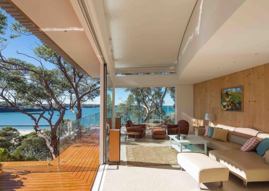 a living room with a glass wall and a deck overlooking a body of water