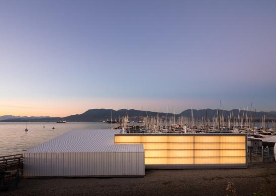 a building with lights on the side and a body of water with boats in the background