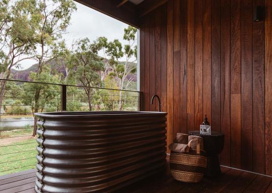 a tub outside with a wood wall and a toilet