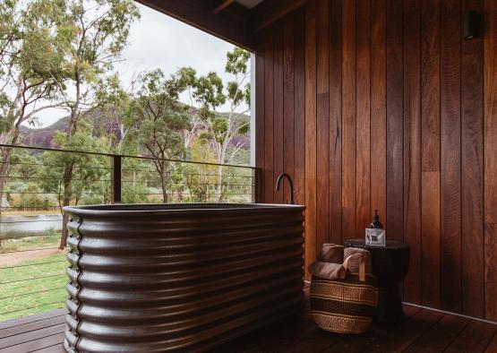 a tub outside with a wood wall and a toilet