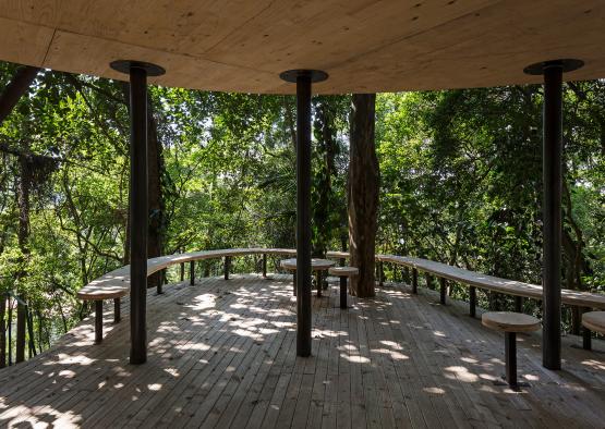 a wooden deck with benches and a canopy in the woods