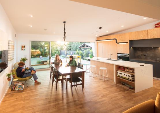 a group of people sitting around a table in a room with a kitchen and dining table