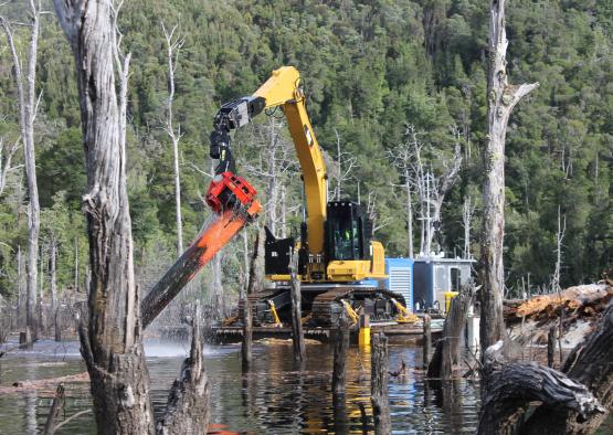 a yellow and black machine in water with trees in the background