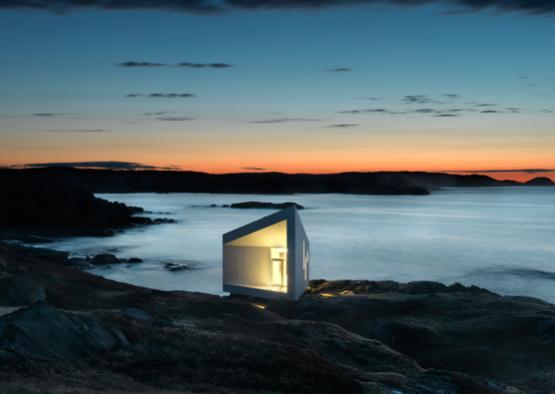 a small white building on a rocky shore with water in the background