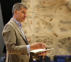 Man holding a notebook while speaking to an audience