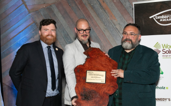 Man handing award made of reclaimed timber to two men standing against timber wall