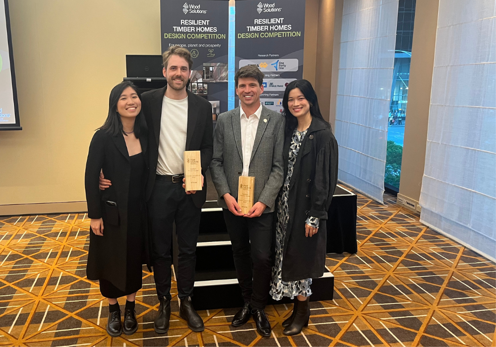 Four people standing together with the two men in the middle holding their award trophies
