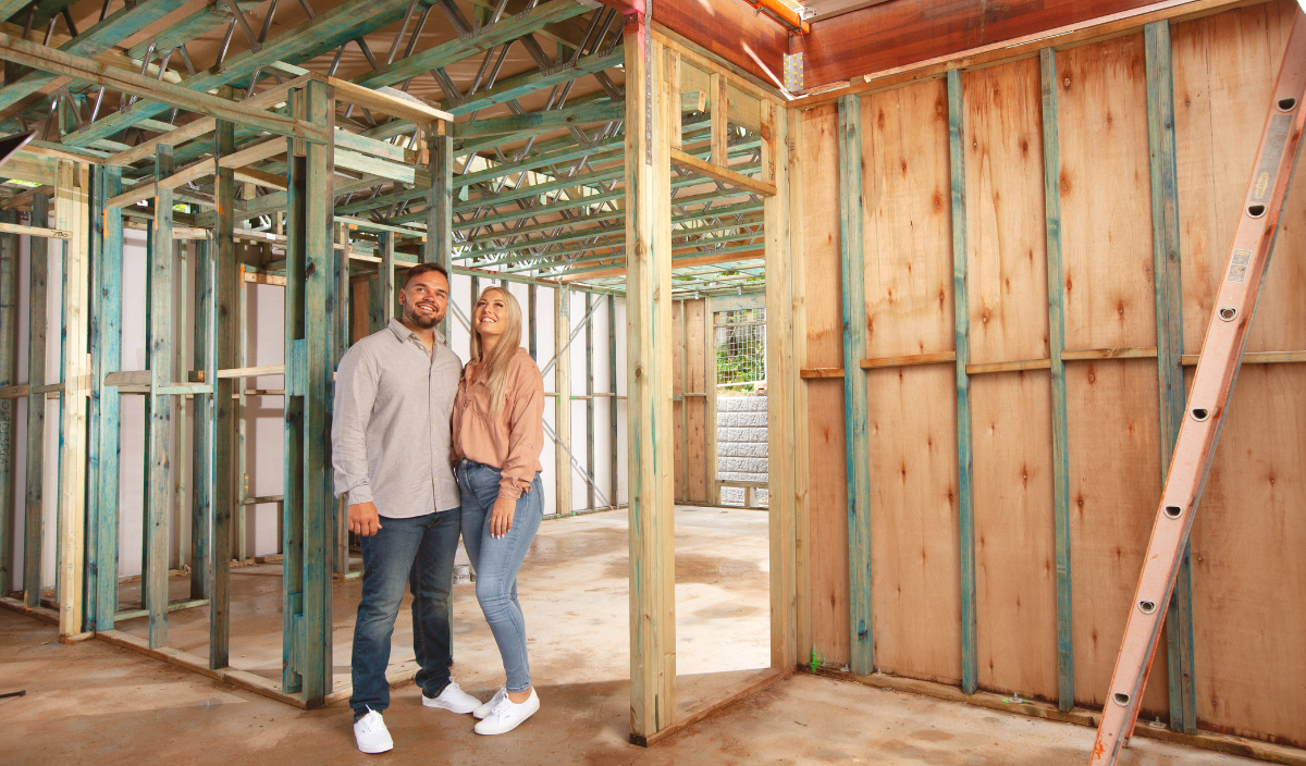 A man and woman standing among the timber framing of their newly built home