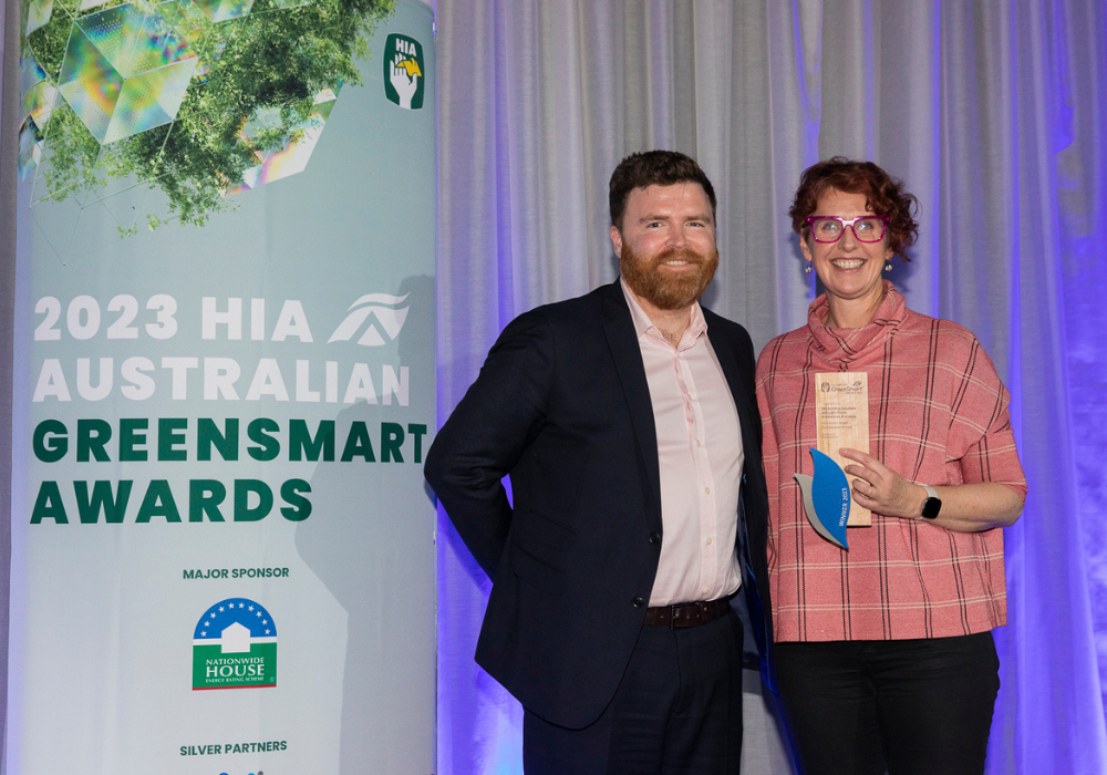 Two people standing against an HIA GreenSmart Awards banner with one holding an award