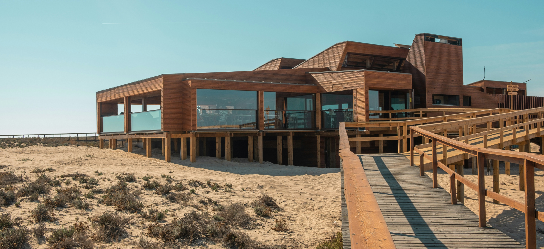 Deck entrance to timber community centre on sandy beach with native grasses