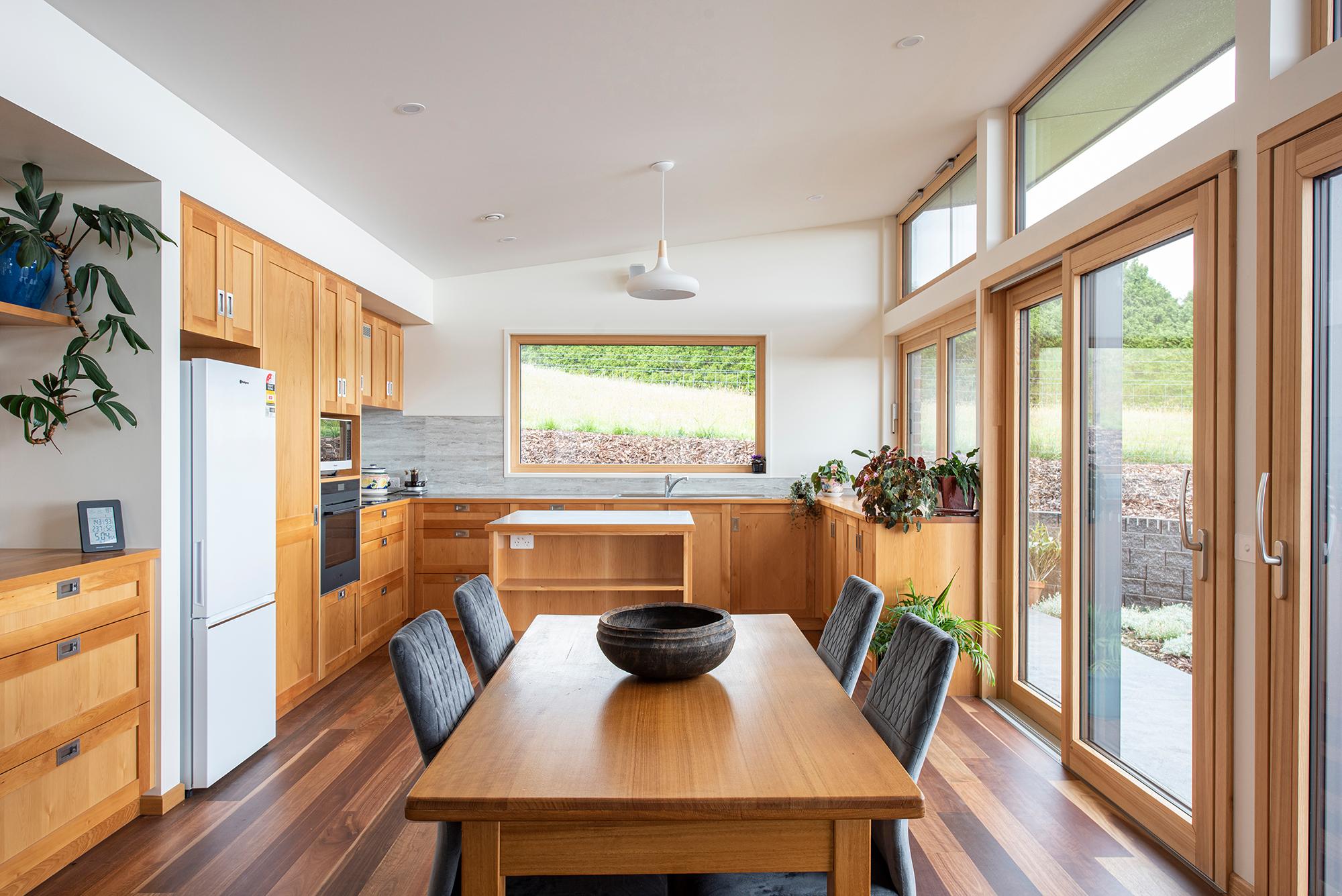 Interior shot of kitchen with timber surfaces, table, and floors
