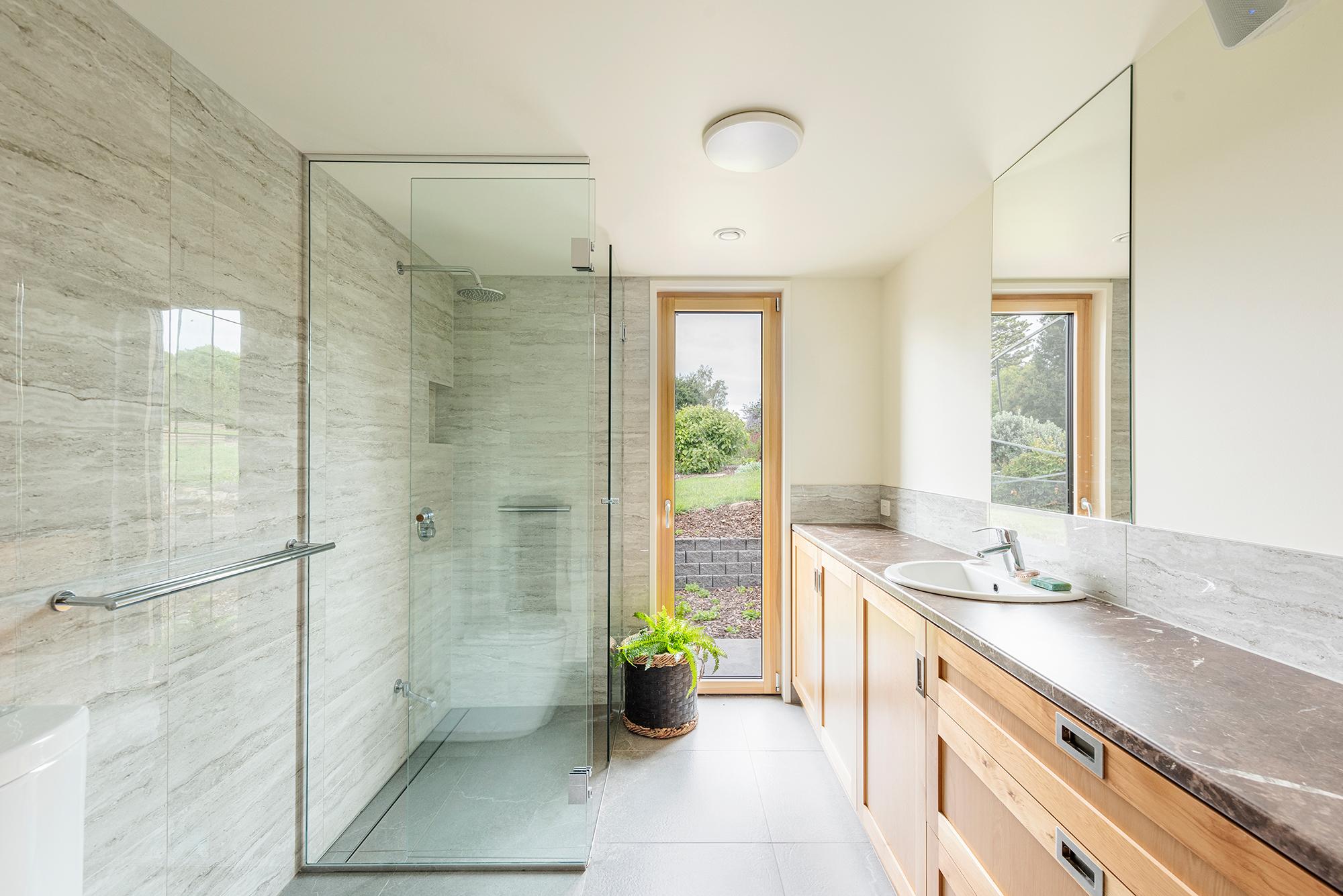 Shot of looking through bathroom with large glass shower and timber cabinets