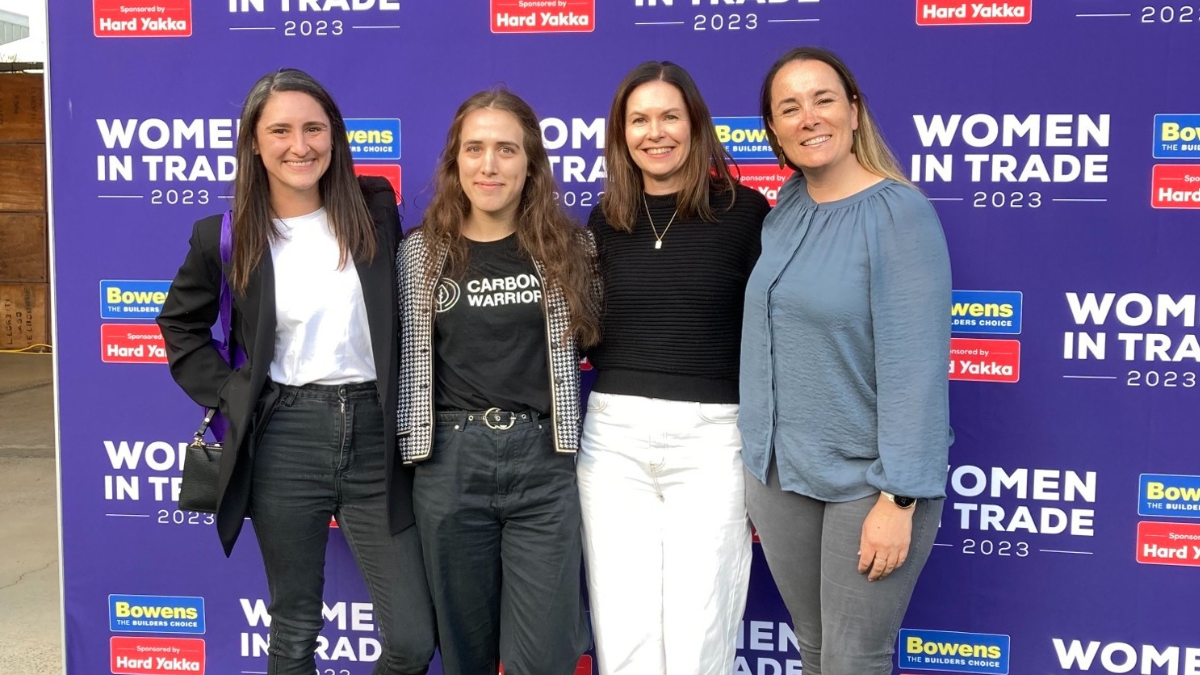 Four women posing in front of purple media wall