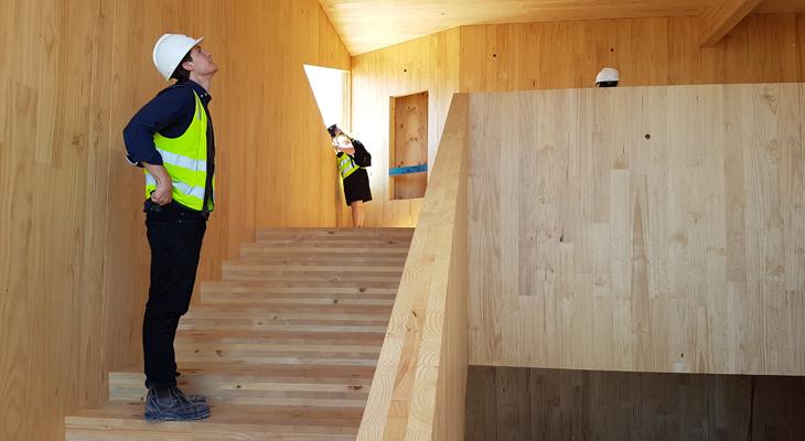 a man in a safety vest and helmet looking up at a wooden staircase