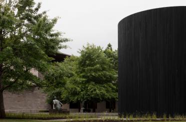a black cylinder with a statue in the background